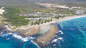 Vue aérienne d’une station balnéaire comprenant plusieurs bâtiments, une plage et une côte rocheuse.