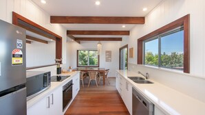 Une cuisine moderne avec des meubles blancs, des poutres en bois et une grande fenêtre donnant sur un paysage verdoyant.