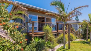 Une maison moderne dotée d’une terrasse en bois, entourée de plantes tropicales et de palmiers.