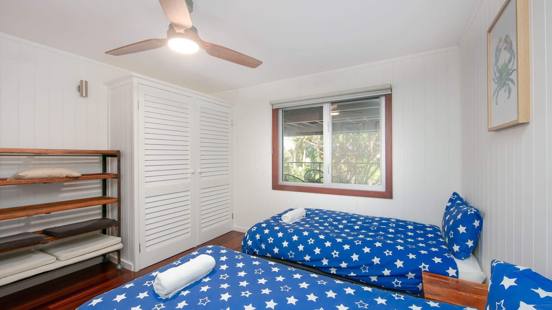 Un dormitorio con dos camas, ventilador de techo, ventana con vistas y armario.