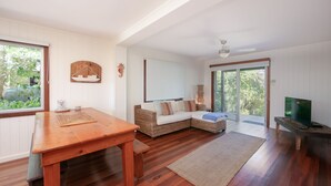 A spacious room with a wooden dining table, a wicker sofa, and a television on a wooden stand. - Pacifica 2 - Brooms Head (Brooms Head)