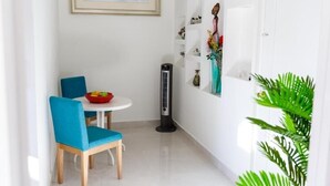 A small dining area with a table and chairs, a standing heater, and a wall-mounted shelf with decorative items. - Hidden Paradise Penthouse overlook Tropical Garden neatPalm Beach (Noord)