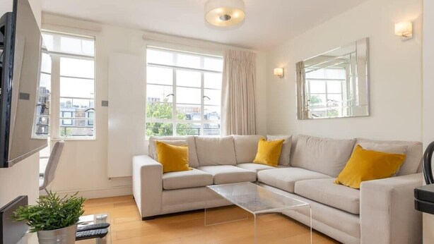 Una sala de estar moderna con un sofá seccional color beige, una mesa de centro de vidrio y un ventanal con cortinas.