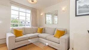 Una sala de estar moderna con un sofá seccional color beige, una mesa de centro de vidrio y un amplio ventanal con cortinas.