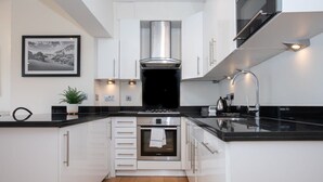 Una cocina moderna con armarios blancos, una campana extractora de acero inoxidable, horno empotrado y encimera negra.