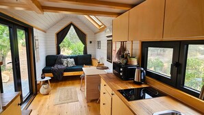 Una cocina compacta y moderna con estufa integrada, un comedor con banco y un amplio ventanal con vistas a zonas verdes.