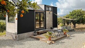 Una casa moderna y compacta con terraza, mobiliario exterior y vistas al huerto circundante.
