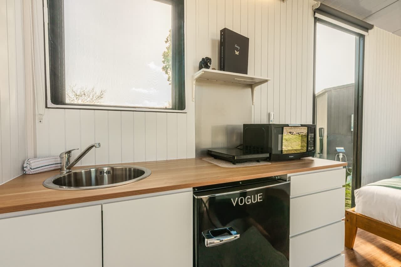 Una cucina compatta con lavello, lavastoviglie, forno a microonde e un piccolo ripiano con un libro e un oggetto decorativo.
