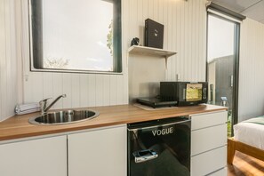 A compact kitchen with a sink, a dishwasher, a microwave, and a small shelf with a book and a decorative item. - Rimu View 1 by Tiny Away (Ruatapu)