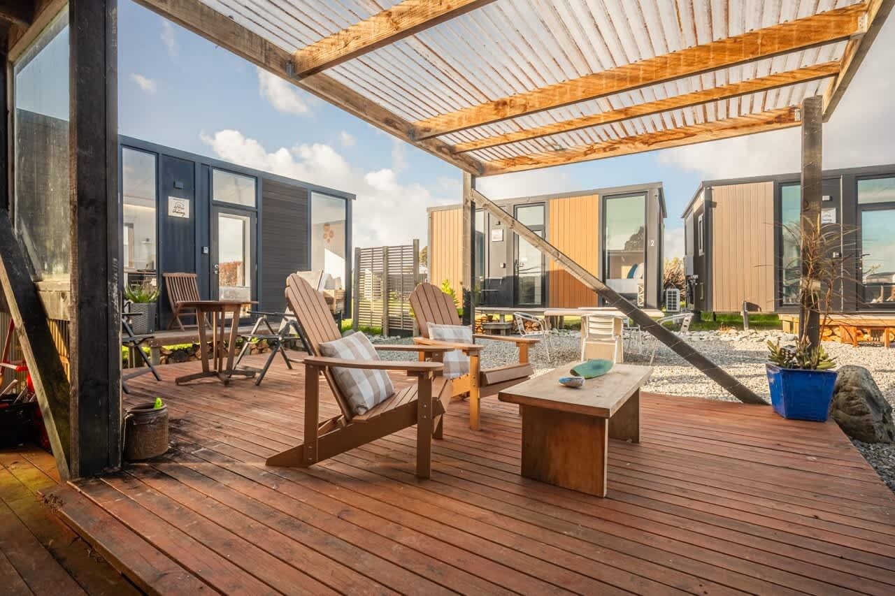 Eine Holzterrasse mit Sitzgelegenheiten im Freien, darunter Stühle und ein Tisch, mit Blick auf ein modernes Gebäude mit großen Fenstern.
