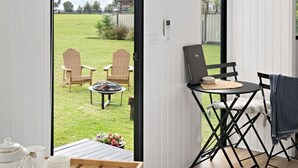 A room with a large sliding glass door leading to a grassy outdoor area, a small table with a teapot and cup, and a folding chair. - Tiny Charm by Tiny Away (Lake Charm)
