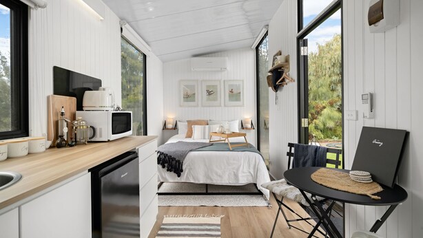 A modern, compact bedroom with a bed, bedside tables, a small desk, and a view of the outdoors. - Tiny Charm by Tiny Away (Lake Charm)