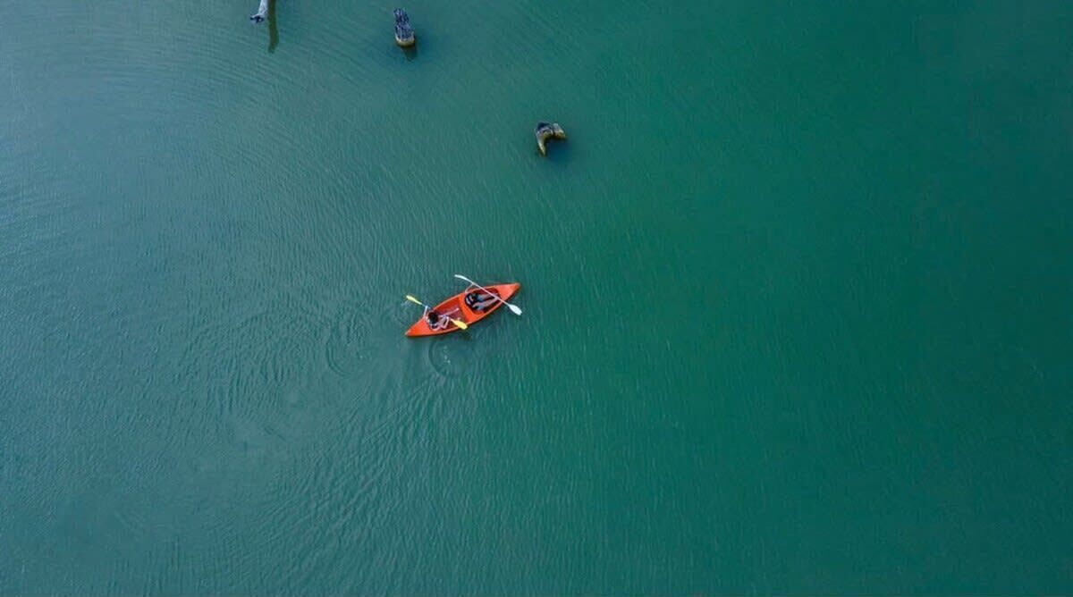 Een luchtbeeld van een rustig waterlichaam met een enkele kajak in het midden.