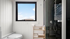 A compact bathroom with a toilet, a shelf with towels, and a shower area. - Tiny Charm by Tiny Away (Lake Charm)