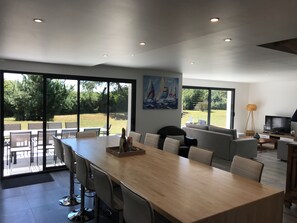 A modern dining area with a long table and chairs, a painting on the wall, and a view of the outdoors. - Gite de la Presqu'île du Golfe du Morbihan (Sarzeau)