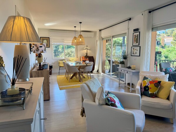 A spacious living room with a dining area, large windows, and a balcony.