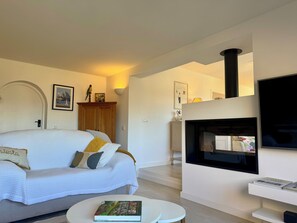 A living room with a sofa, a round coffee table with a book, a fireplace, and a TV.