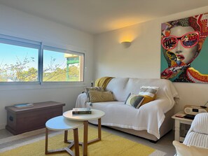 A modern living room with a sofa, a small round table, a bookshelf, and a large window.