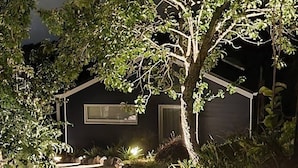 A house with a stone pathway leading to the entrance, surrounded by lush greenery and illuminated by soft lighting. - Huntsbury Hideaway, Cottage with amazing views (Christchurch)