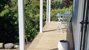 A wooden deck with a table and chairs, surrounded by greenery and hills in the background. - Huntsbury Hideaway, Cottage with amazing views (Christchurch)