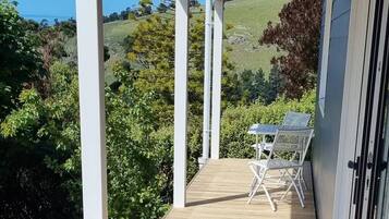 A wooden deck with a table and chairs, surrounded by greenery and hills in the background.