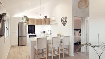 A modern kitchen with a central island, wooden chairs, and pendant lighting.