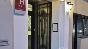 Entrada d'edifici amb una porta de vidre, un senyal d'alarma d'incendis i una lluminària fixada a la paret.