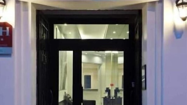 Entrada d'hotel amb una porta de vidre, una recepció i un espai interior visible amb un mostrador i cadires.