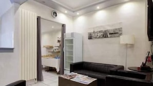 Un saló modern amb un sofà de pell negra, una taula de centre i una televisió. Hi ha una prestatgeria i una porta que condueix a una altra habitació.