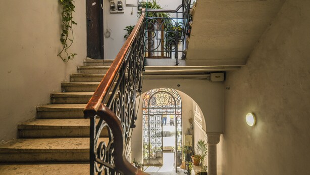 Un escalier orné d’une rampe en fer forgé menant à une porte en arc de cercle.
