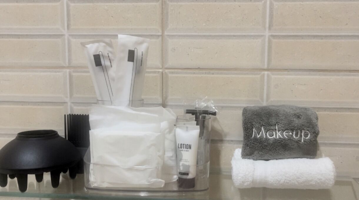 Ein Badezimmer-Waschtisch mit einem Handtuch für Kosmetik, einer schwarzen Haarbürste, einem weißen Handtuch und einem durchsichtigen Behälter, der eine Lotiontube und eine schwarze Haarbürste enthält.