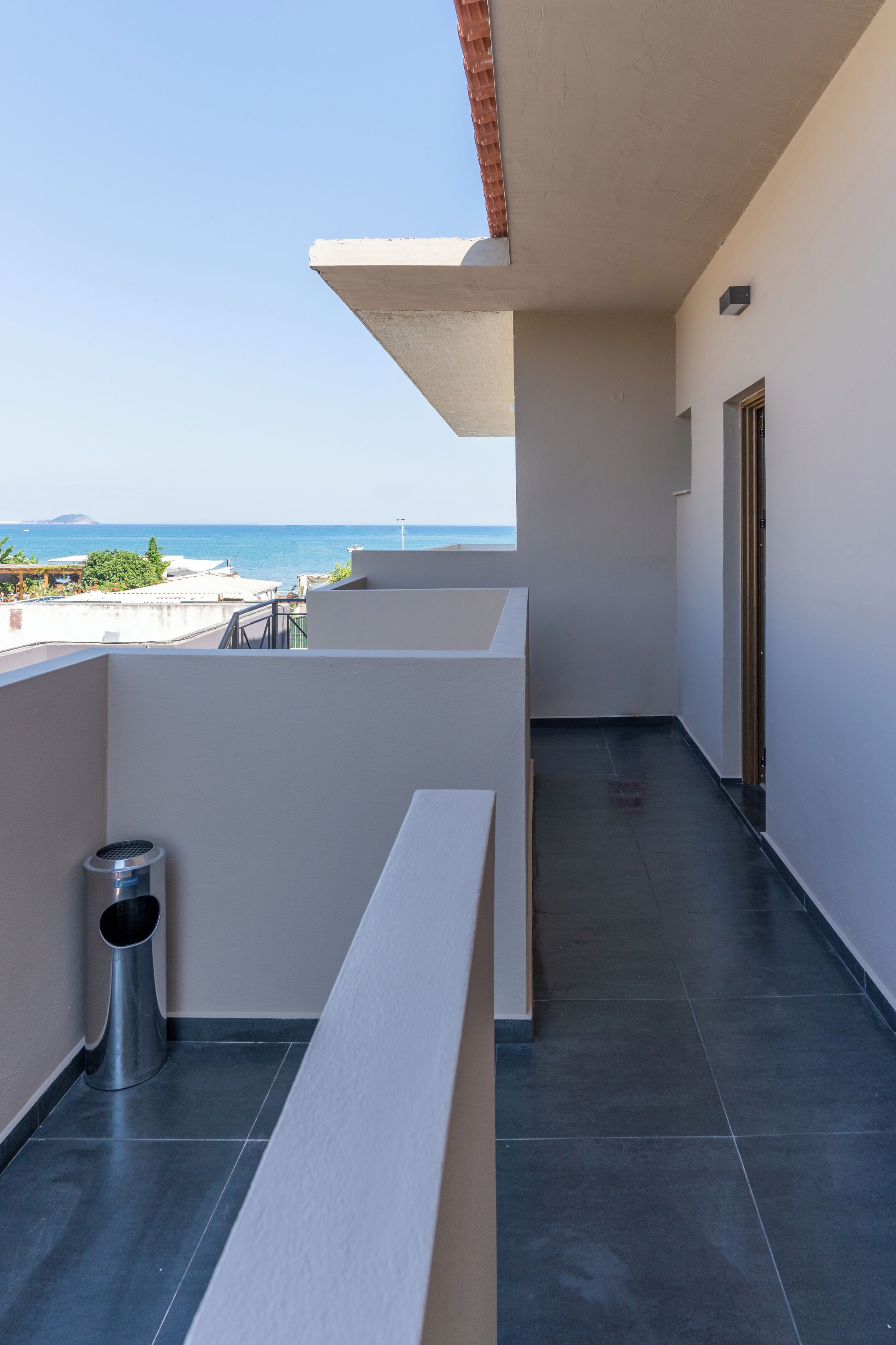 A balcony with a view of the sea, a trash bin, and a door.