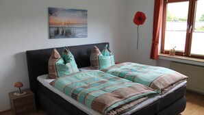 A bedroom with a bed, a nightstand, a lamp, a window with curtains, and a painting on the wall. - Holiday Home Rehsiepen near Winterberg (Schmallenberg)
