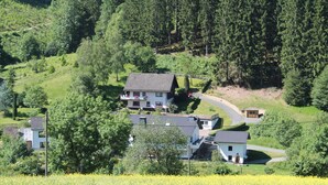 A rural house with a sloped roof, surrounded by dense forest and a field of yellow flowers. - Holiday Home Rehsiepen near Winterberg (Schmallenberg)