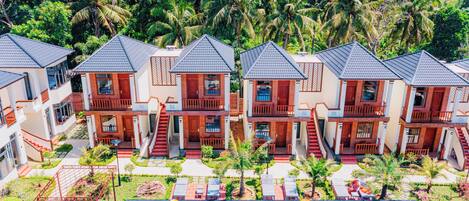 A resort with multiple bungalow-style buildings, a central swimming pool, and lush tropical vegetation.