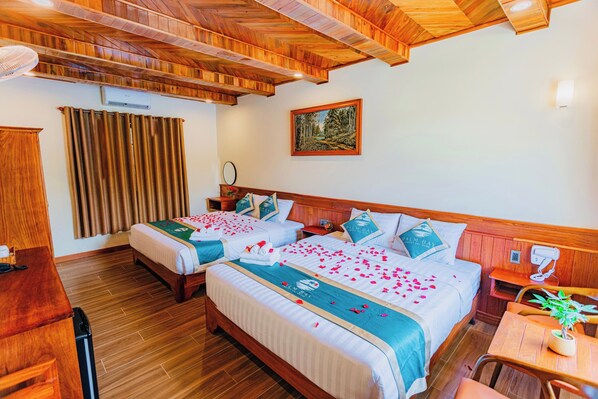 Habitación de hotel con dos camas, piso de madera, ventilador de techo, un cuadro y un escritorio con teléfono.