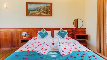 A hotel room with a bed adorned with a towel swan centerpiece, a framed painting on the wall, and a wooden headboard.