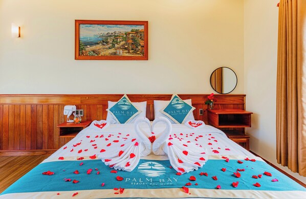 Una habitación de hotel con una cama decorada con una grúa de toalla en el centro, un cuadro en la pared y un cabecero de madera.
