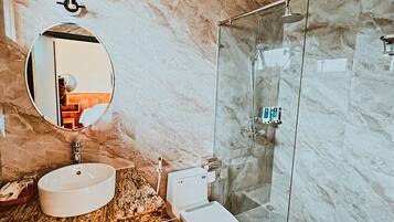 A bathroom with a marble wall, a round mirror, a sink, a toilet, and a glass shower enclosure.