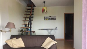 A living room with a brown sofa, a small wooden table, a ladder, a hanging lamp, and a painting on the wall. - Duplex in Caparica (Caparica)