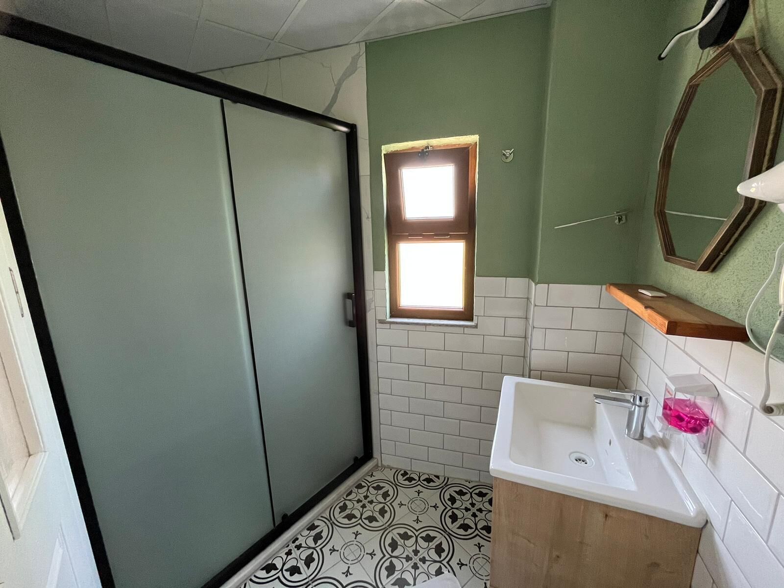 A bathroom with a shower, a sink, and a window.