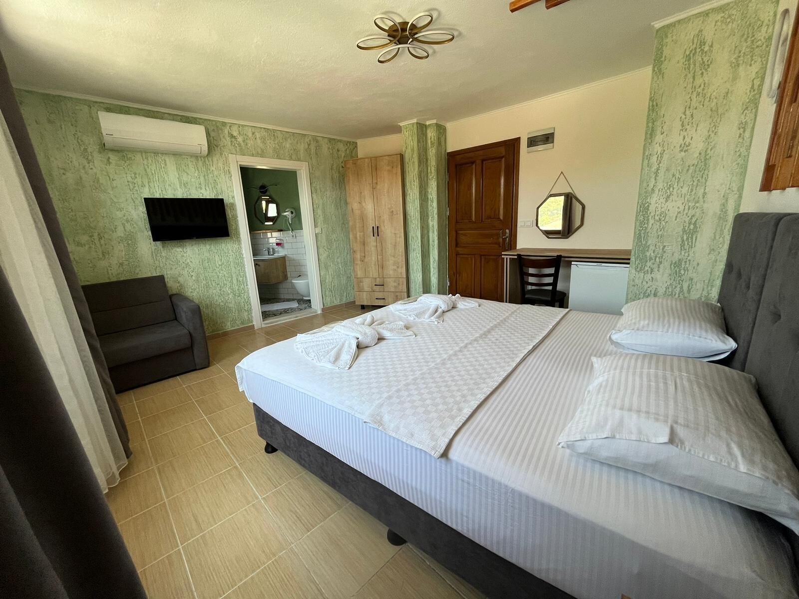 A bedroom with a large bed, a TV mounted on the wall, a desk with a chair, and a wardrobe.