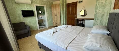 A bedroom with a large bed, a TV mounted on the wall, a desk with a chair, and a wardrobe.
