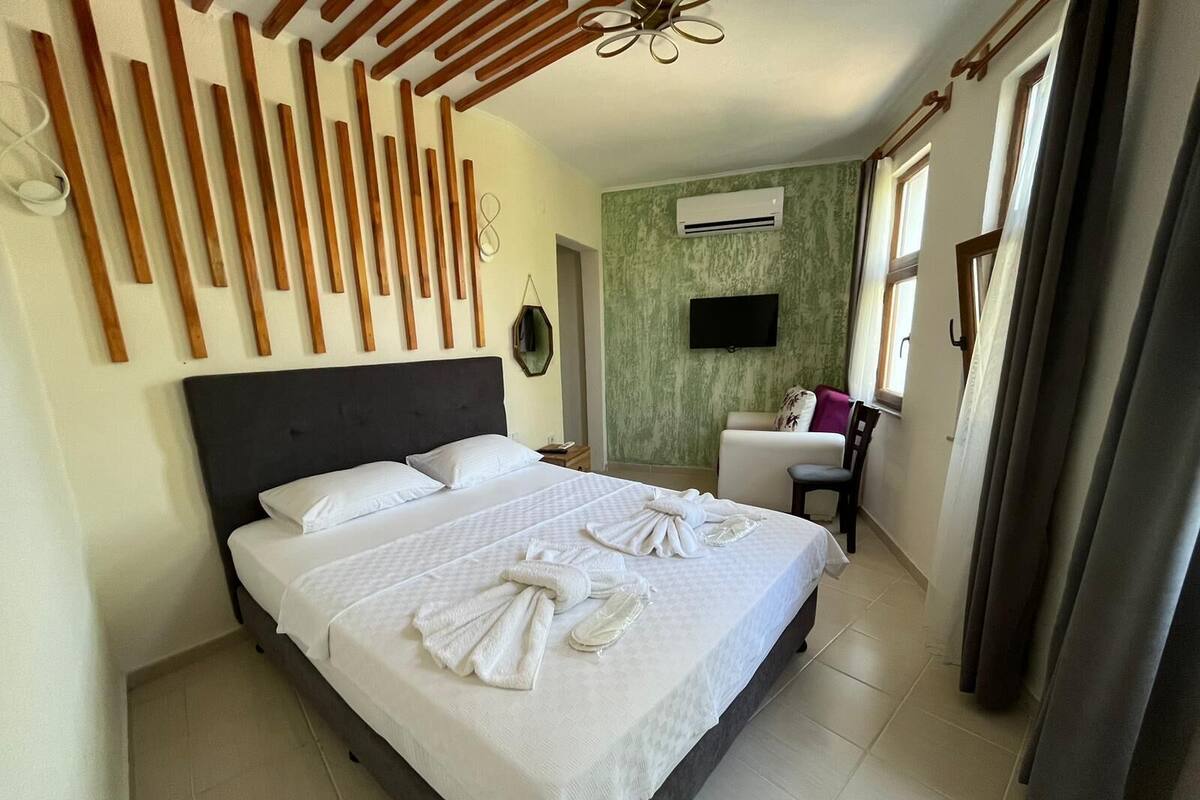 A hotel room with a large bed, a flat-screen TV, an air conditioning unit, and a chair.