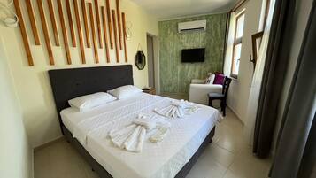 A hotel room with a large bed, a flat-screen TV, an air conditioning unit, and a chair.