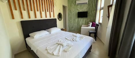 A hotel room with a large bed, a flat-screen TV, an air conditioning unit, and a chair.