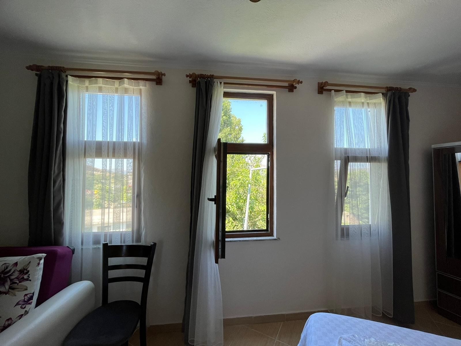 A room with a bed, a chair, and two windows with curtains.