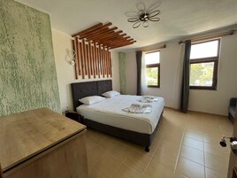 A bedroom with a bed, a wooden desk, a ceiling fan, and two windows.