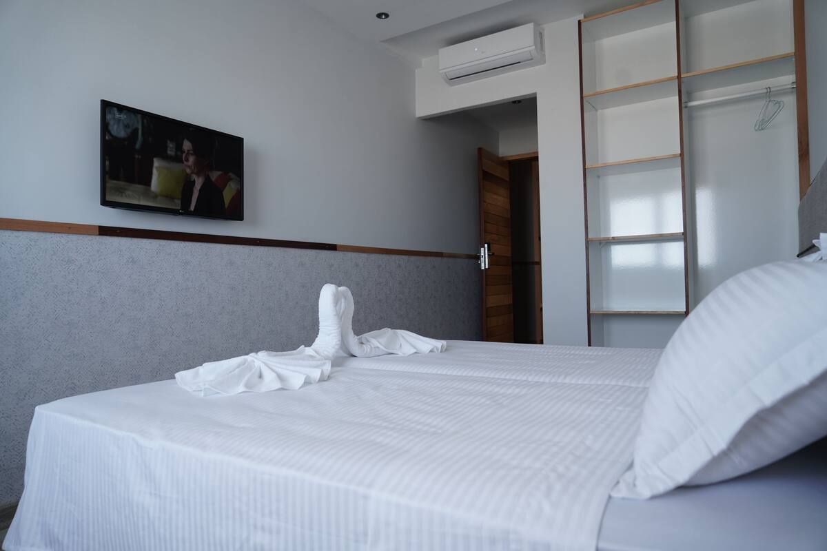 Una habitación de hotel con una cama bien hecha, un televisor de pantalla plana montado en la pared y un armario con puertas correderas.