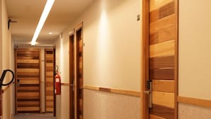 A hotel hallway with wooden doors, a fire extinguisher, and a corridor leading to another room. - Hôtel Seashell (Oualidia)